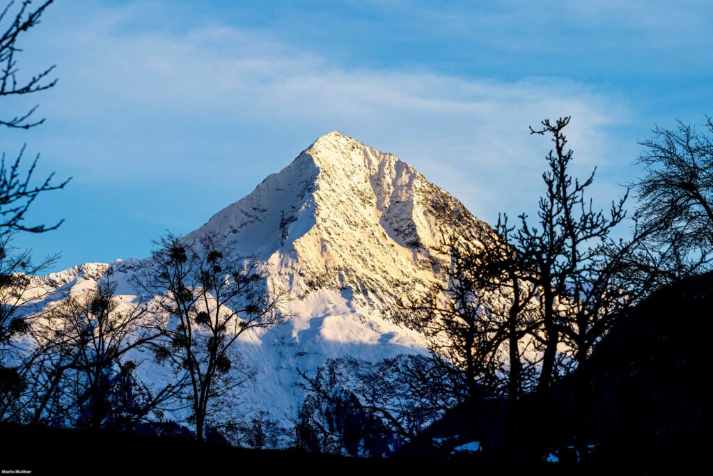 Bristen, das markante Wahrzeichen des Kantons Uri, präsentiert sich in einer winterlichen Pracht. Das Bild zeigt das majestätische Bergmassiv, das von einer Schneedecke bedeckt ist und sich gegen den klaren blauen Himmel abhebt.