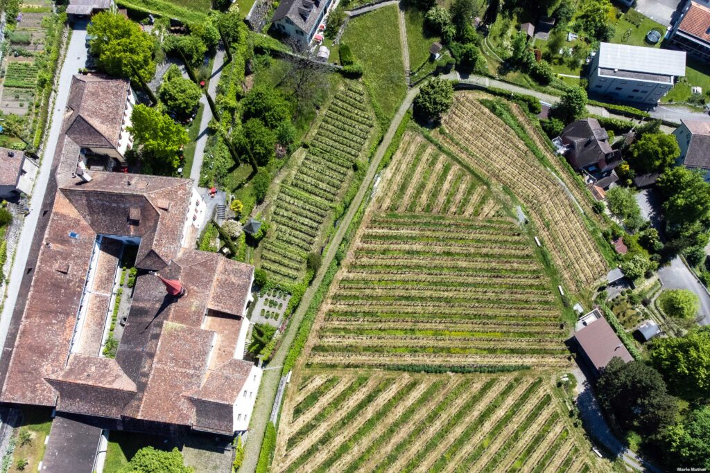 Die Drohnenfotografie fängt das Kapuzinerkloster in Altdorf, Kanton Uri, aus der Vogelperspektive ein. Das Kloster ist eine beeindruckende historische Struktur mit einer reichen spirituellen und kulturellen Bedeutung. Das Bild zeigt das Klostergebäude, das von grünen Gärten und einem gepflegten Innenhof umgeben ist.