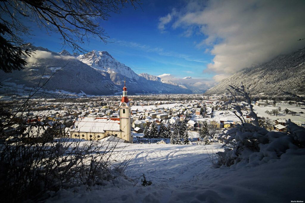 Die Kirche von Schattdorf im Winter mit Blick auf den Gitschen im Kanton Uri. Das Bild fängt die idyllische Atmosphäre des Dorfes ein, während die Kirche als zentrales Element im Vordergrund steht.